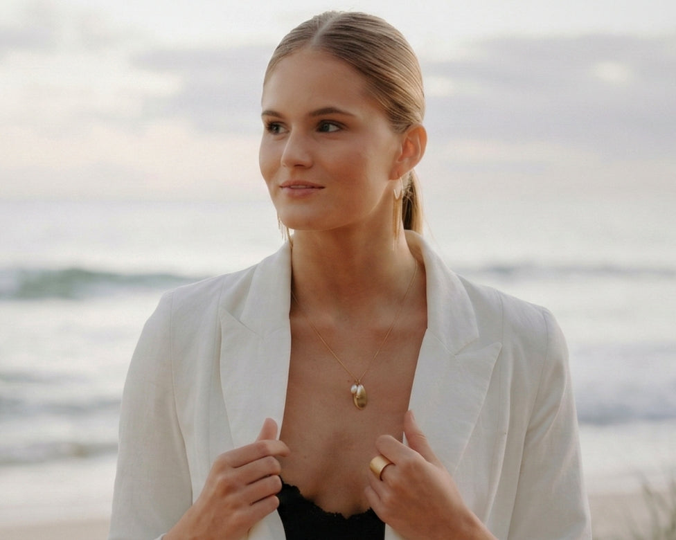 Woman in a white blazer standing by a body of water
